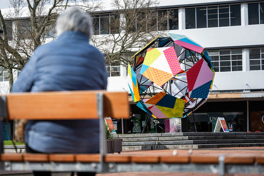 A lady sits on a bench in front of a sculpture in Hamilton Square that is part of the 
