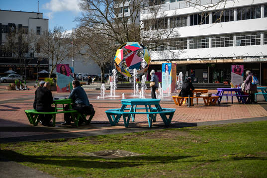 People sit on benches in front of a sculpture in Hamilton Square that is part of the 
