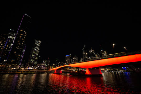 A bridge, lit in red, over Yarra River