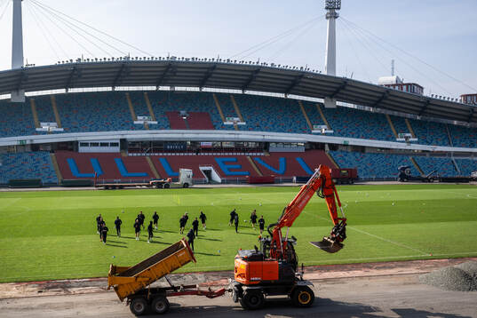 En grävmaskin kör förbi medan spelarna värmer upp