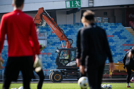 En grävmaskin kör förbi medan spelarna värmer upp