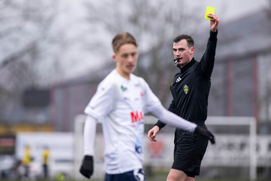 Domare Stjepan Dodik delar ut varning till Åstorps FFs Mio Johansson