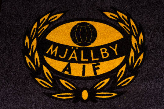 Mjällbys klubbmärke på en matta